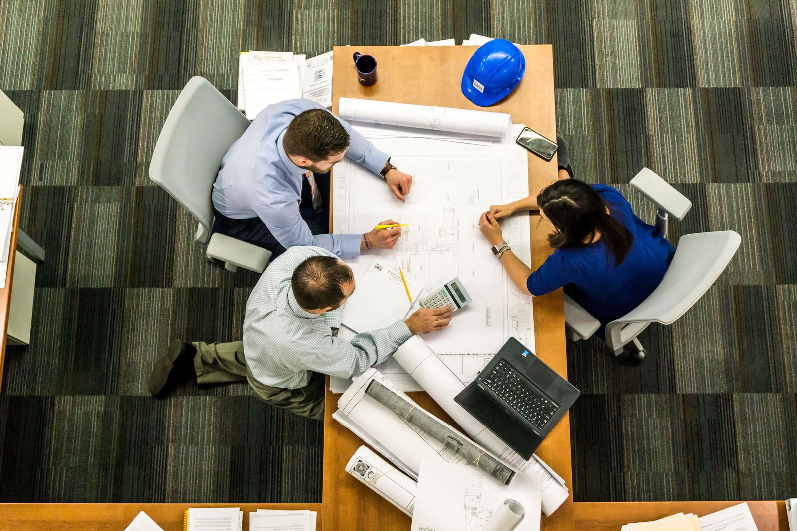 Overhead view of a team planning around a table with drawings and laptops